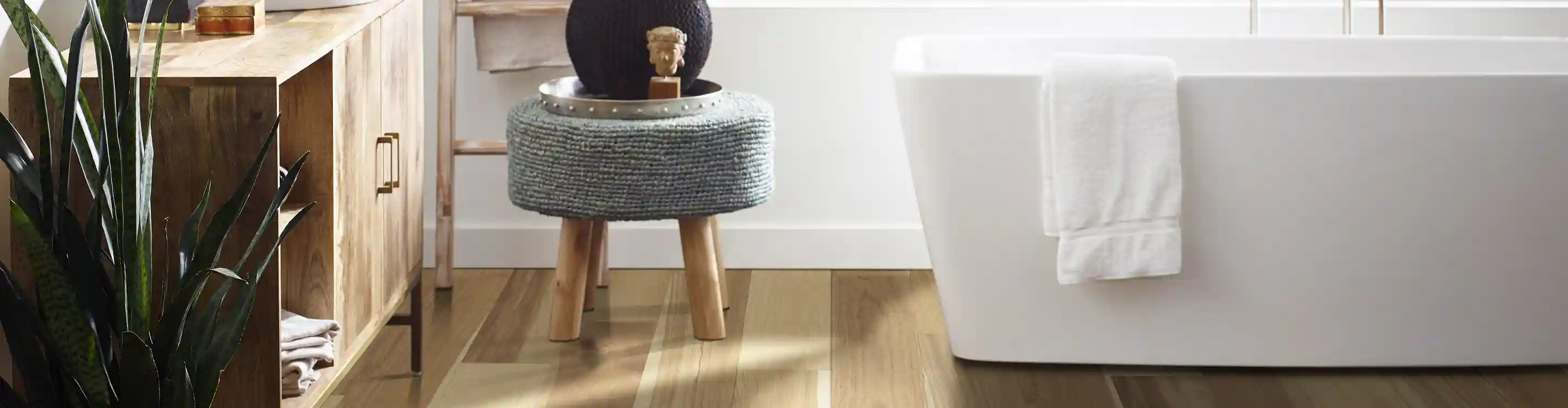 light hardwood flooring in bathroom with white soaker tub and grey stool